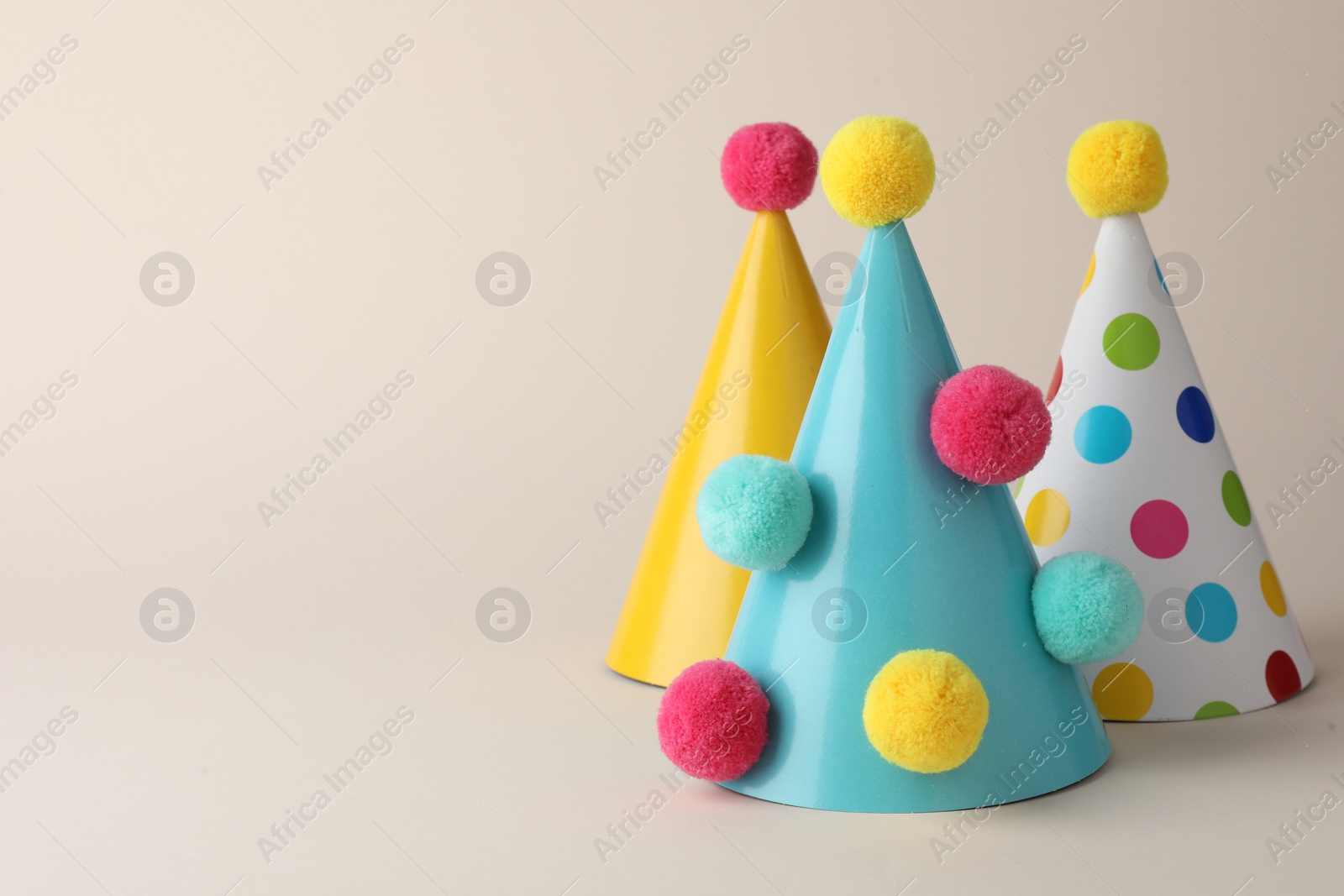 Photo of Colorful party hats with pompoms on beige background. Space for text