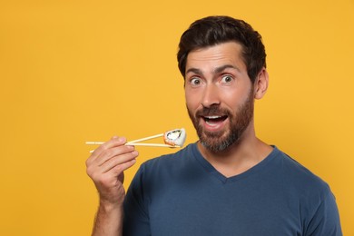 Happy man eating sushi roll with chopsticks on orange background