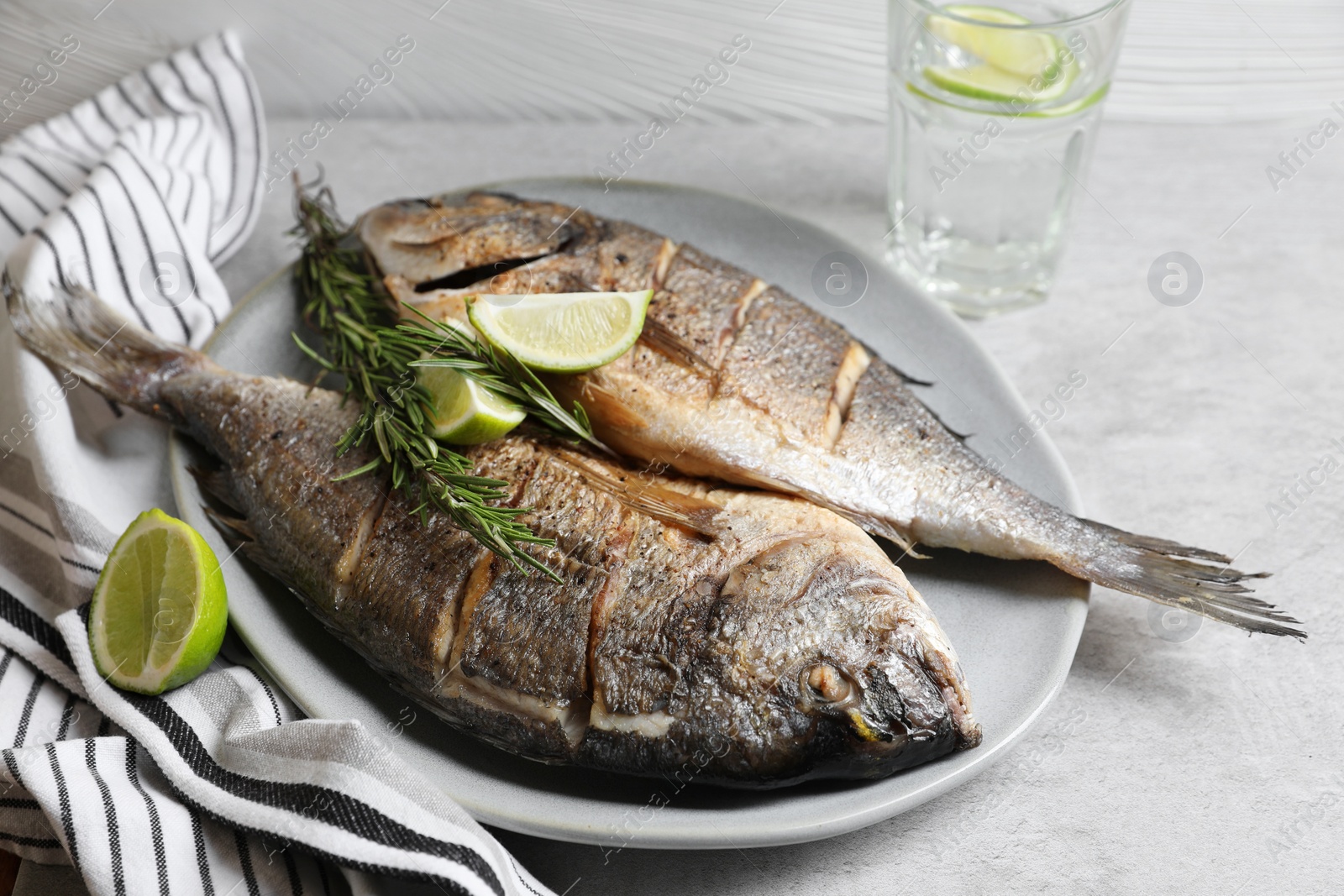 Photo of Delicious baked fish with rosemary and lime on grey table, closeup. Seafood