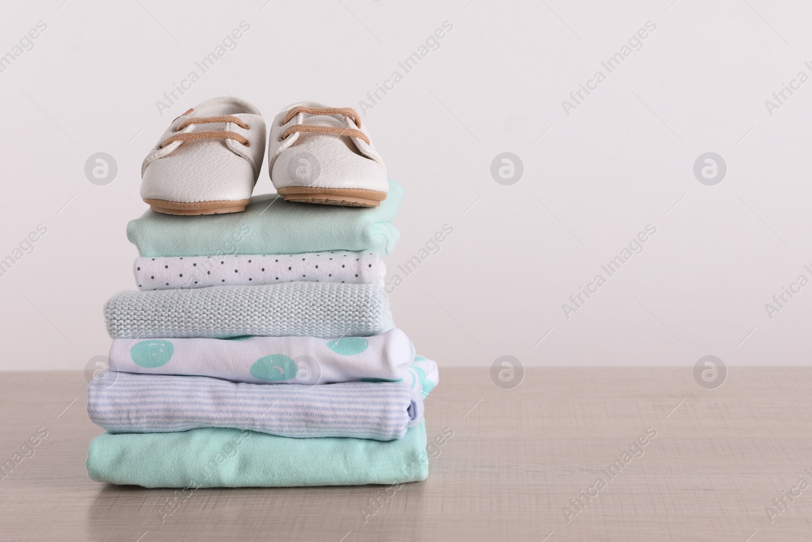 Photo of Stack of baby boy's clothes and shoes on wooden table against white background, space for text