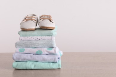 Stack of baby boy's clothes and shoes on wooden table against white background, space for text