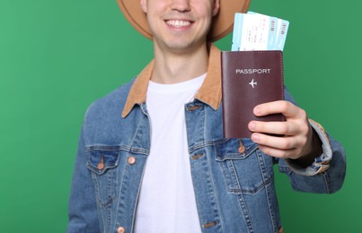 Photo of Smiling man showing passport and tickets on green background, closeup