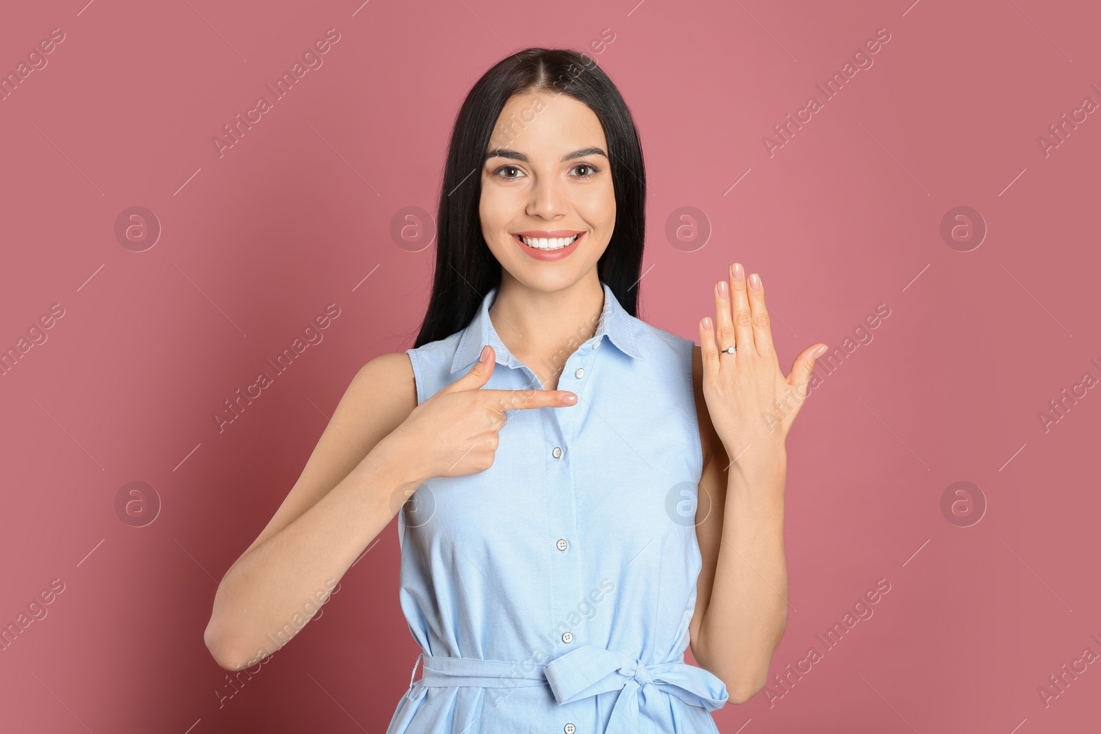 Photo of Happy young woman wearing beautiful engagement ring on pink background