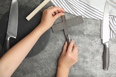 Photo of Woman sharpening knife at grey table, top view