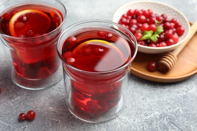 Photo of Tasty hot cranberry tea with lemon in glasses and fresh berries on light grey textured table
