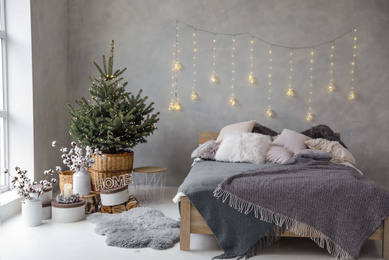 Photo of Little Christmas tree with fairy lights in bedroom interior