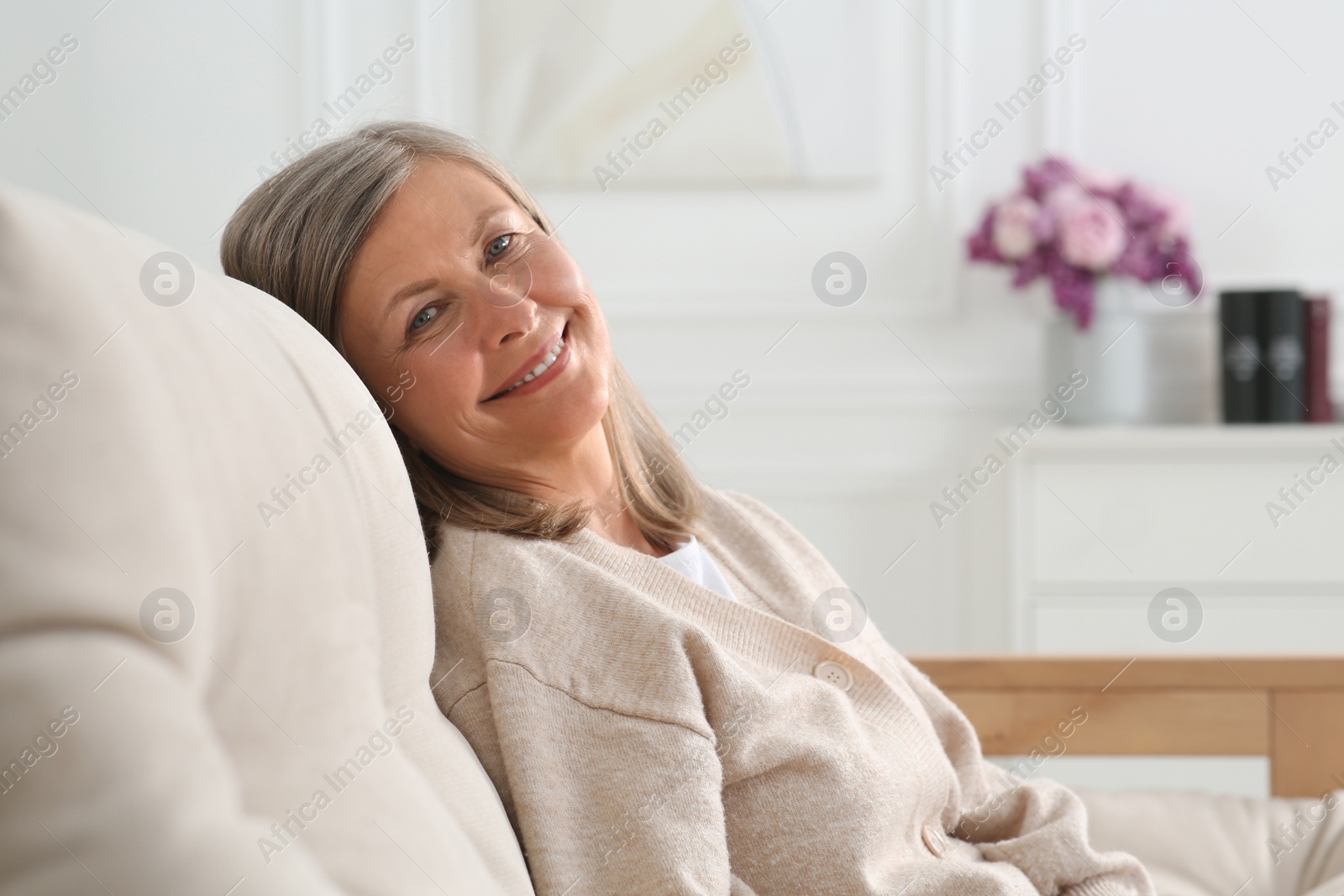 Photo of Beautiful senior woman on sofa at home, space for text