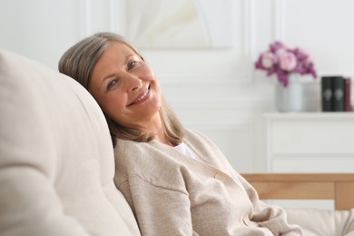 Photo of Beautiful senior woman on sofa at home, space for text