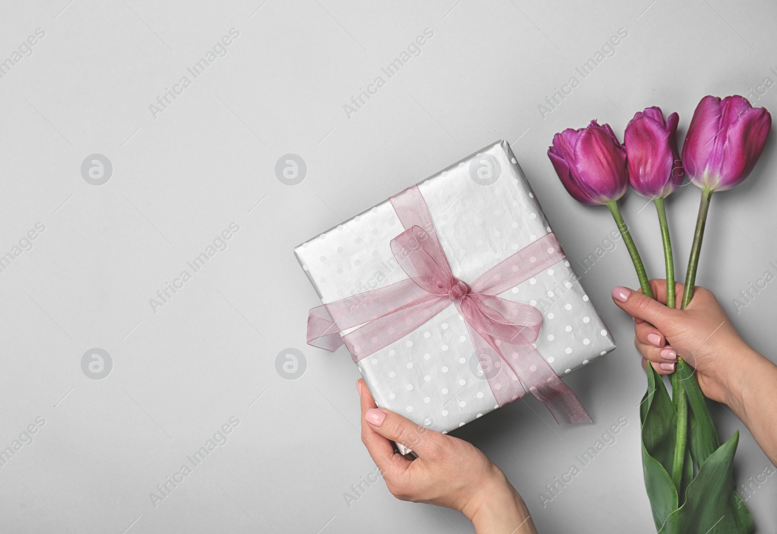 Photo of Woman holding elegant gift box and tulips for Mother's Day on light background, top view