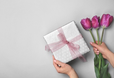 Photo of Woman holding elegant gift box and tulips for Mother's Day on light background, top view