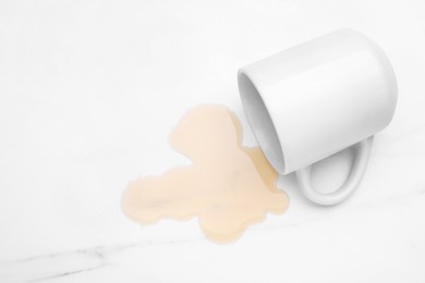 Puddle of liquid and overturned mug on white marble table, above view. Space for text