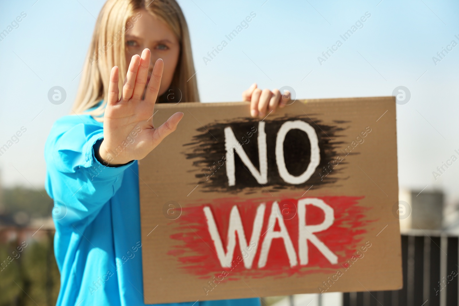 Photo of Sad woman holding poster with words No War and showing stop gesture outdoors