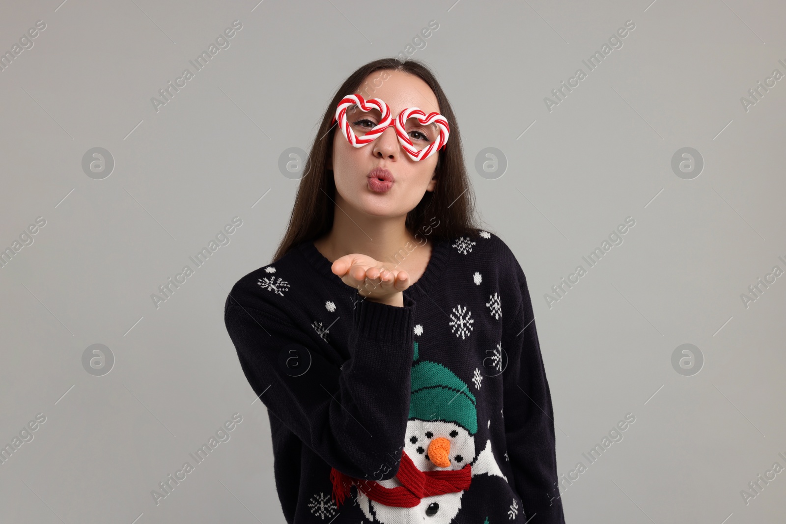 Photo of Happy young woman in Christmas sweater and funny glasses blowing kiss on grey background