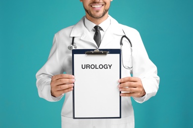 Male doctor holding clipboard with word UROLOGY on turquoise background, closeup