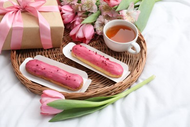 Photo of Tasty breakfast. Delicious eclairs, tea, flowers and gift box on bed