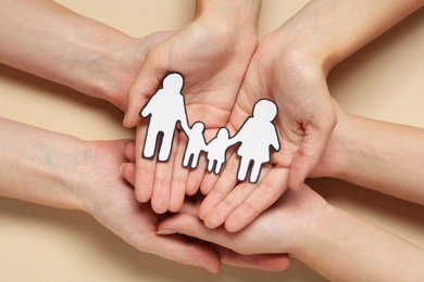 Photo of People holding paper family cutout on beige background, top view