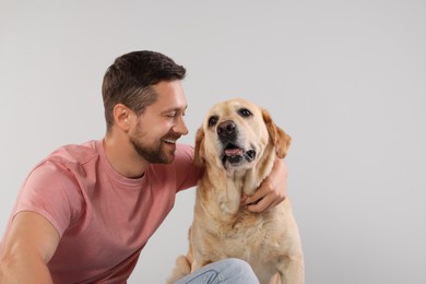 Man hugging with adorable Labrador Retriever dog on light gray background. Space for text