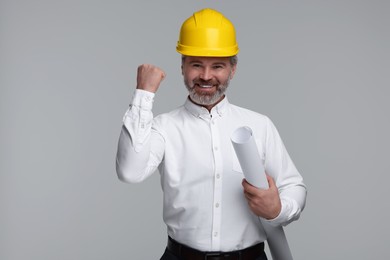 Photo of Architect in hard hat holding draft on grey background