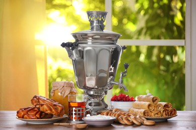 Traditional Russian samovar and treats on wooden table against window in room