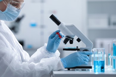 Photo of Young scientist dripping sample onto Petri dish while working with microscope in laboratory.