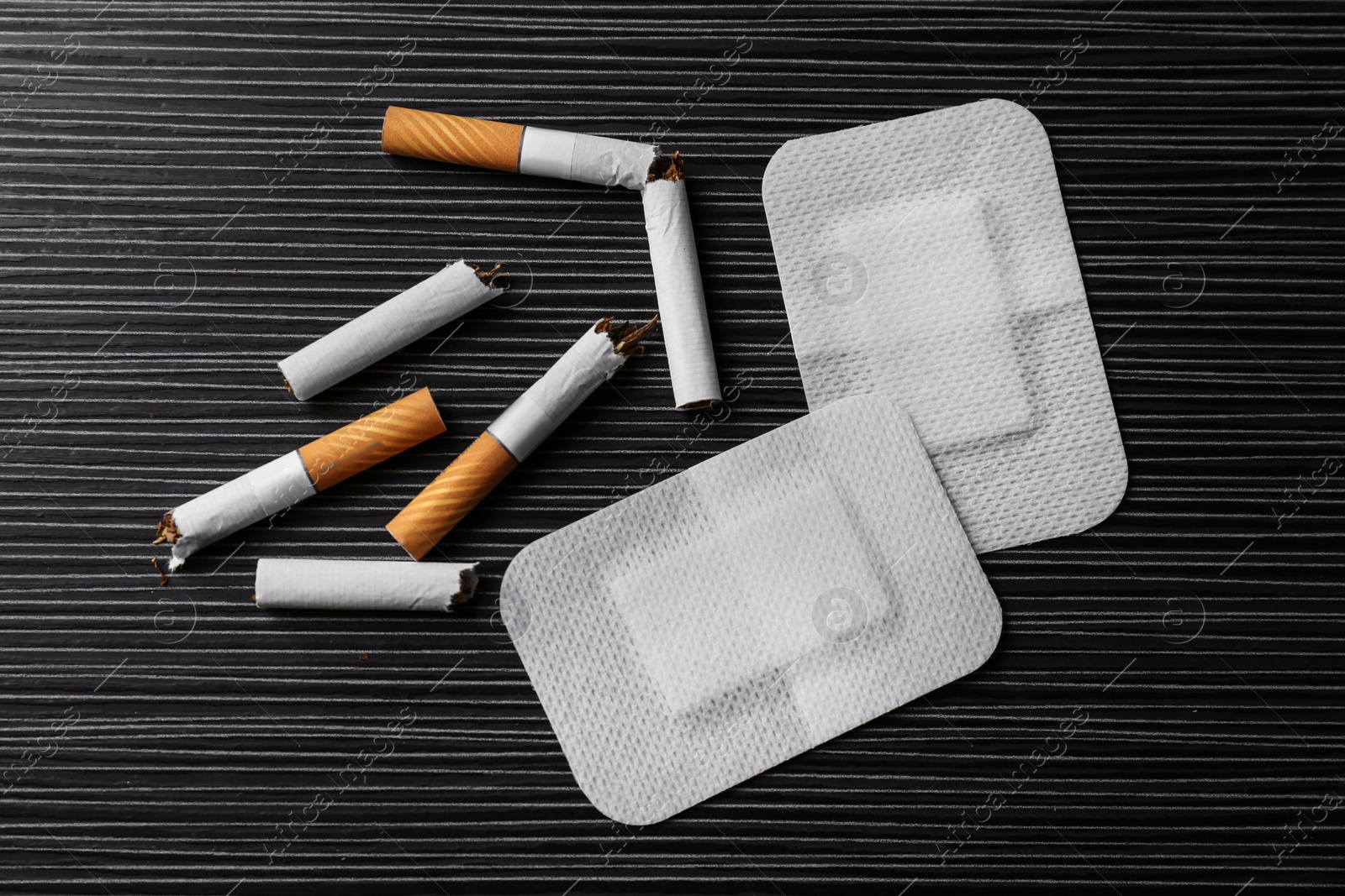 Photo of Nicotine patches and broken cigarettes on black table, flat lay