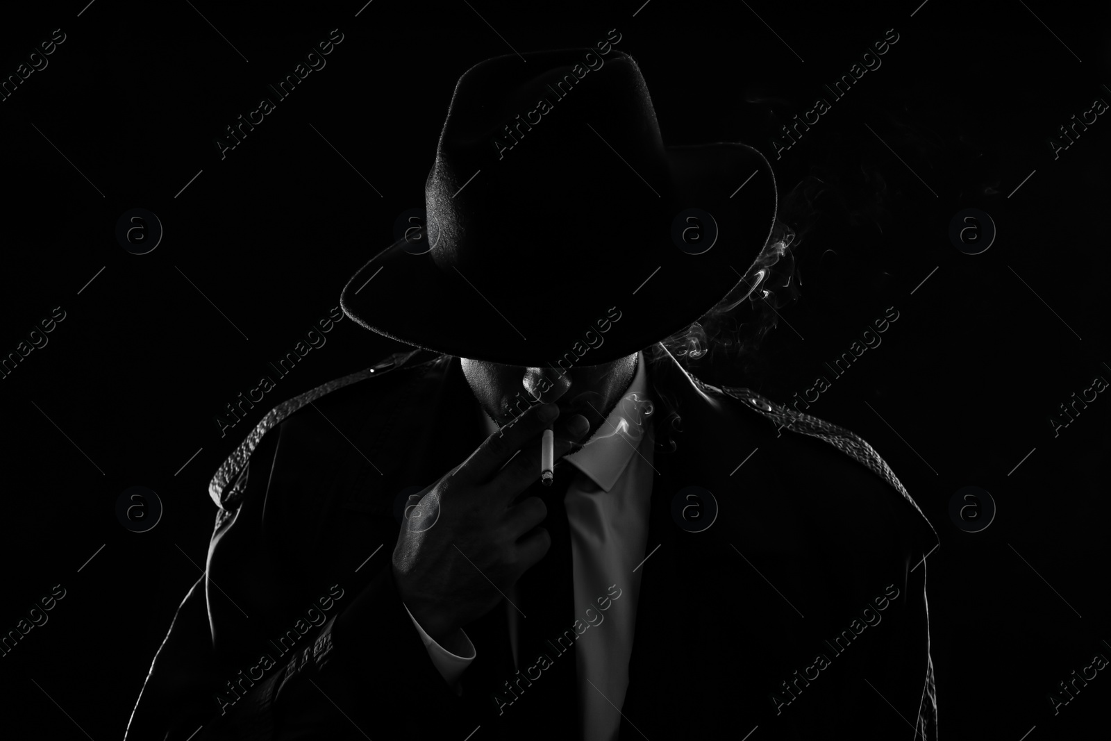 Photo of Old fashioned detective smoking cigarette on dark background, black and white effect