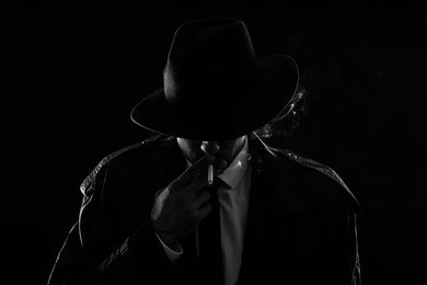 Photo of Old fashioned detective smoking cigarette on dark background, black and white effect