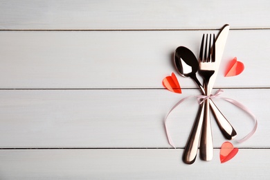 Photo of Cutlery set and pink ribbon on white table, top view with space for text. Valentine's day romantic dinner