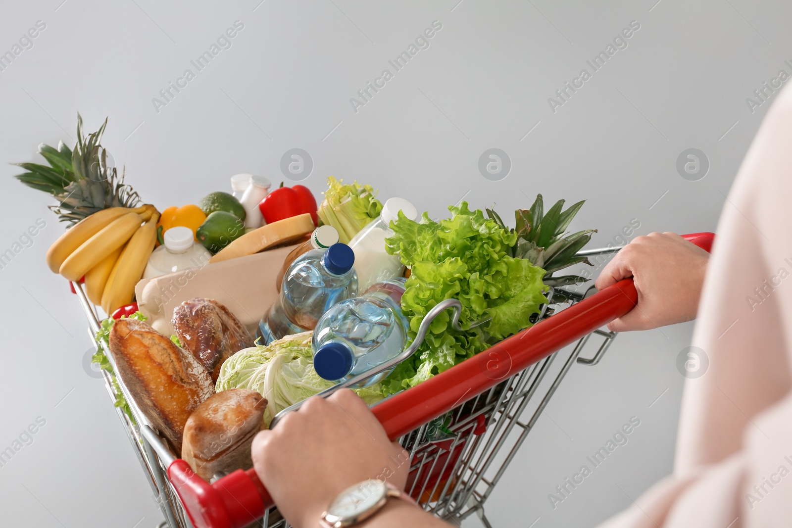 Photo of Woman with shopping cart full of groceries on grey background, closeup