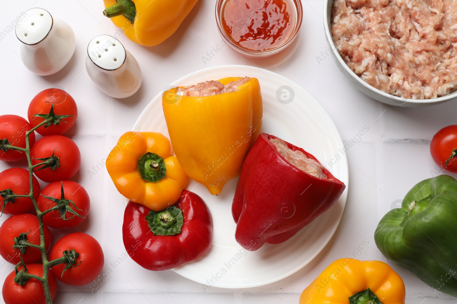 Photo of Raw stuffed peppers, ground meat and ingredients on white tiled table, flat lay