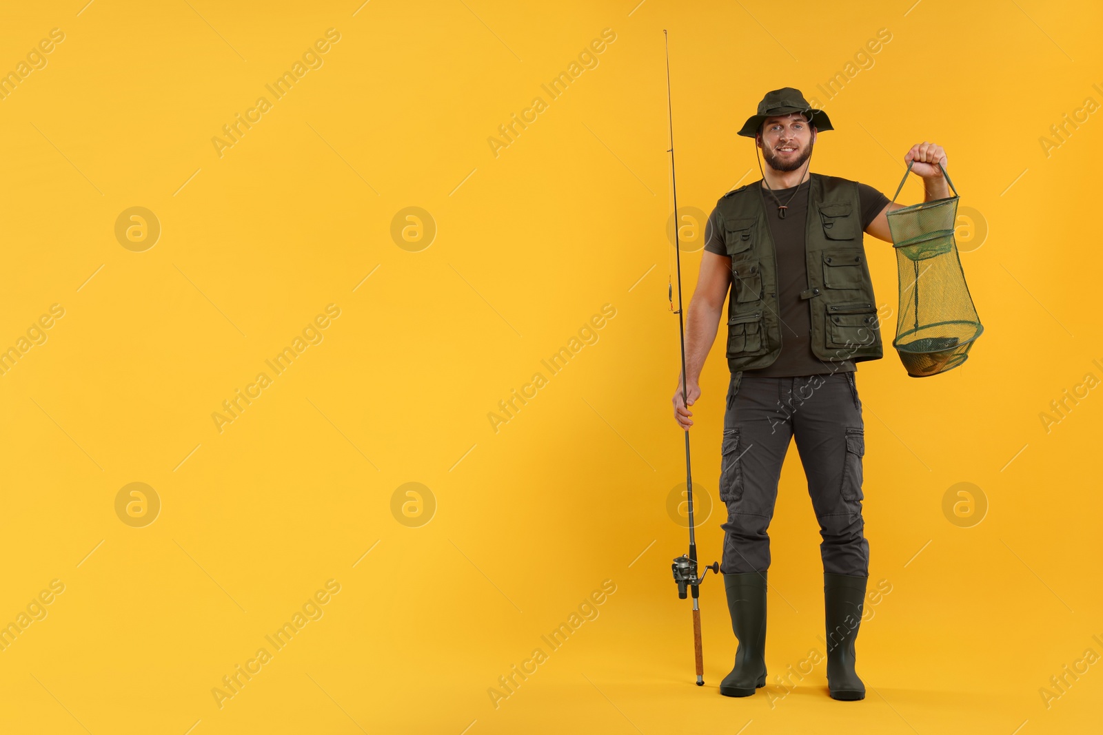 Photo of Fisherman holding rod and fishing net with catch on yellow background, space for text