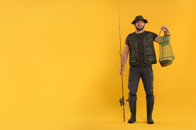 Photo of Fisherman holding rod and fishing net with catch on yellow background, space for text