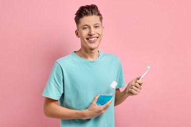 Photo of Young man with mouthwash and toothbrush on pink background