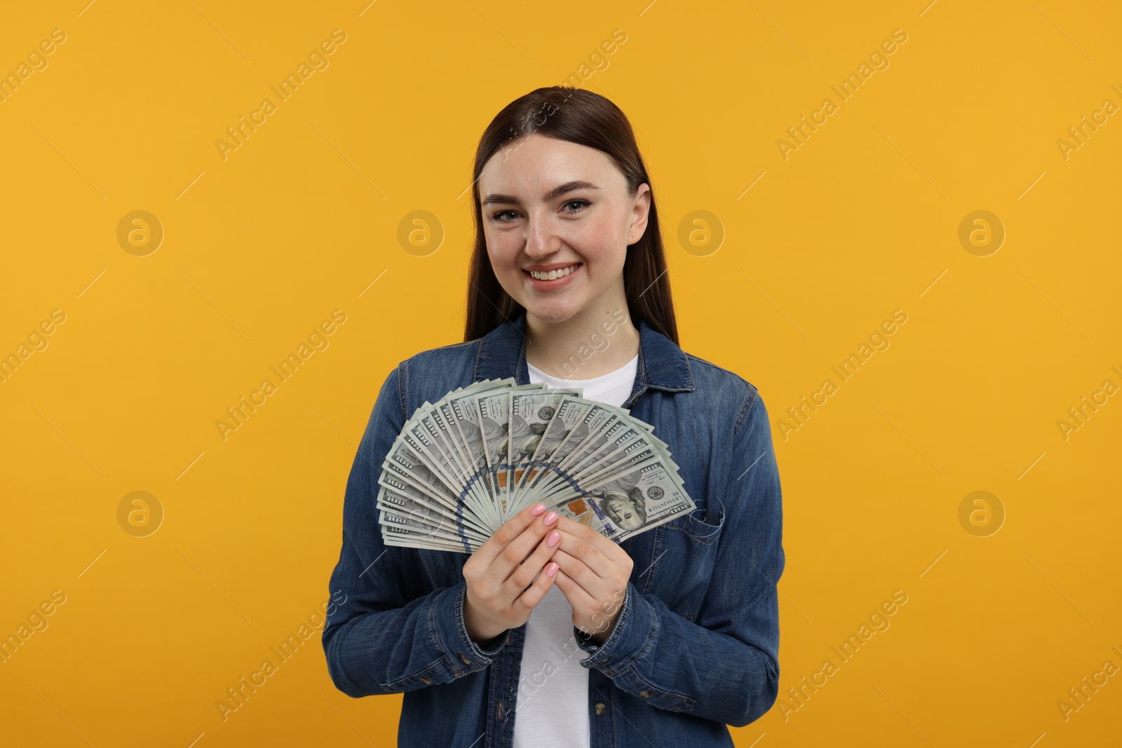 Photo of Happy woman with dollar banknotes on orange background