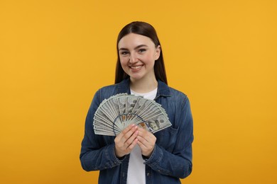 Happy woman with dollar banknotes on orange background