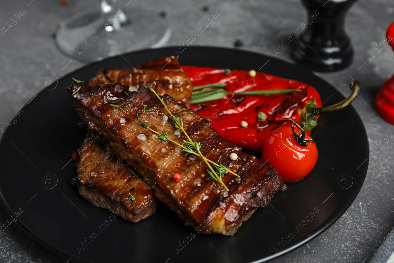 Photo of Plate with grilled meat on grey table, closeup