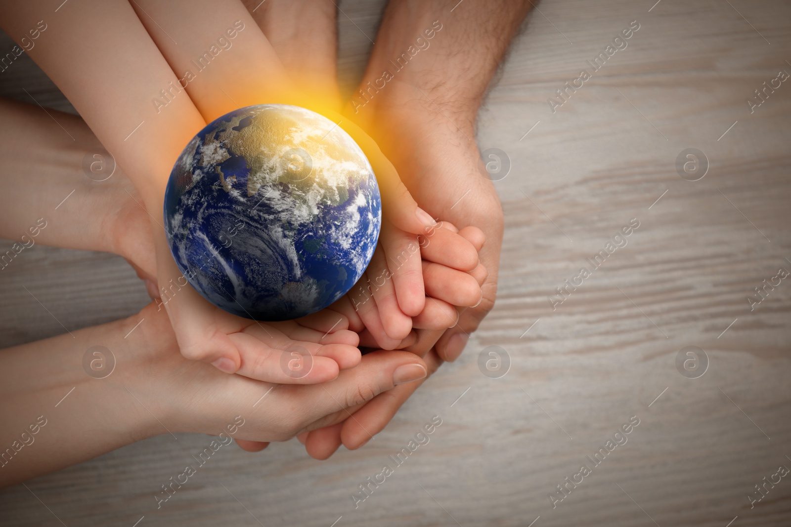 Image of World in our hands. Top view of parents and kid holding digital model of Earth on wooden background, space for text 