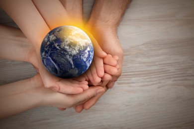 World in our hands. Top view of parents and kid holding digital model of Earth on wooden background, space for text 