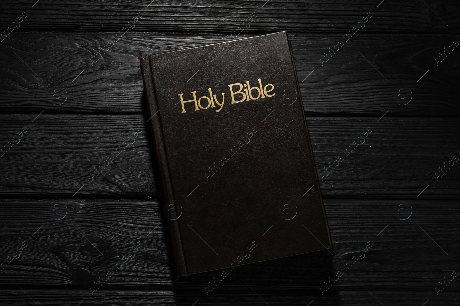 Photo of Bible with dark cover on black wooden table, top view. Christian religious book