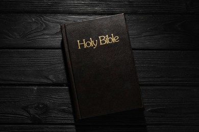 Bible with dark cover on black wooden table, top view. Christian religious book