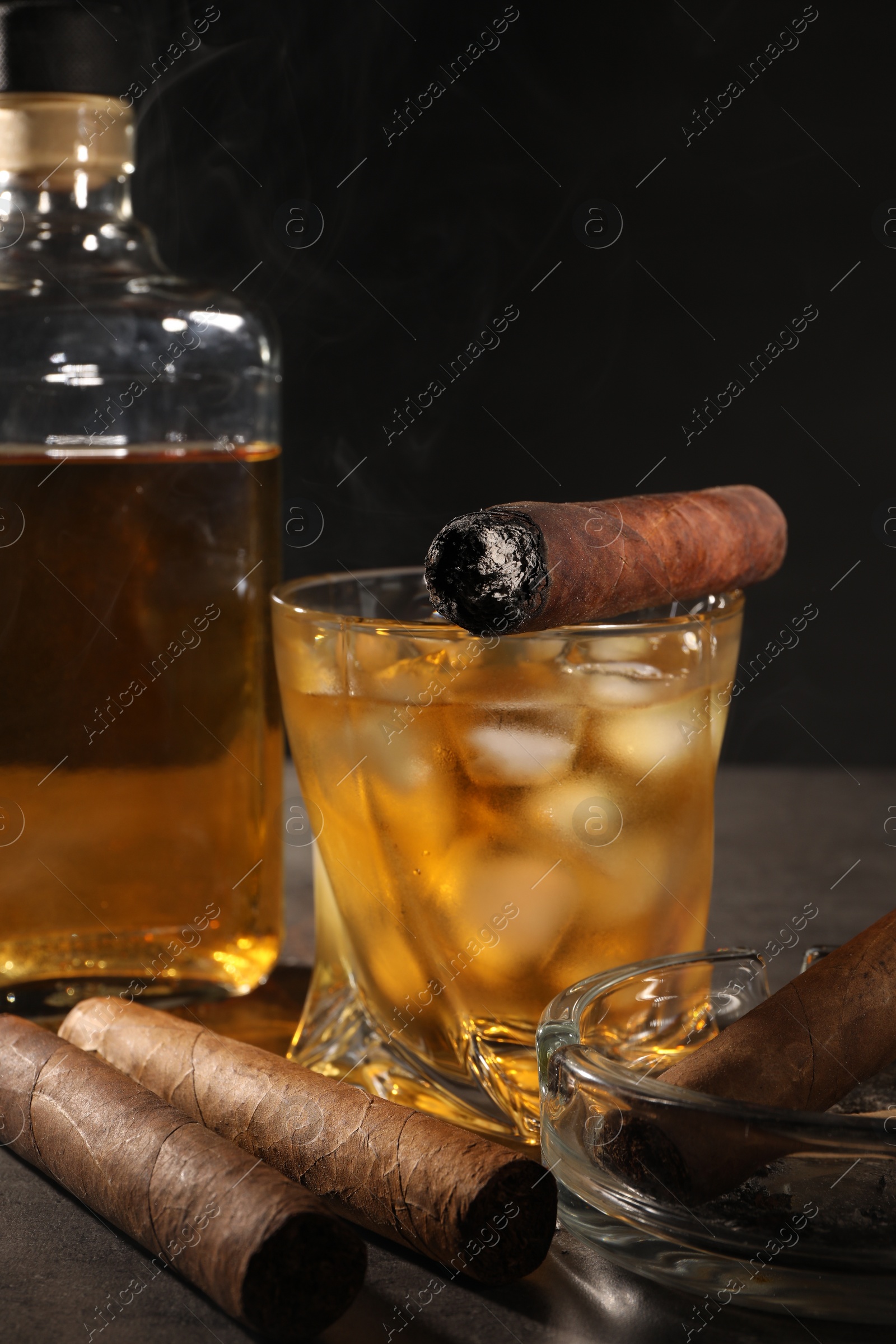 Photo of Cigars and whiskey on grey table against black background