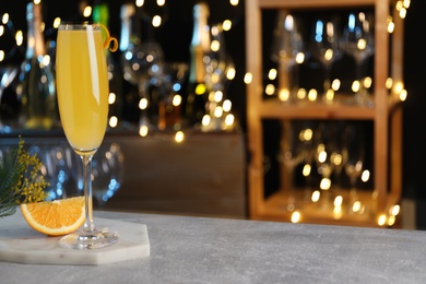 Photo of Mimosa cocktail with garnish and fresh fruit on bar counter against blurred lights, space for text