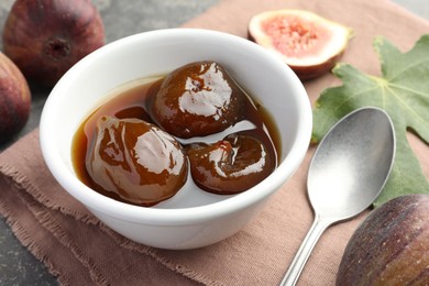 Photo of Bowl of tasty sweet jam, fresh figs and spoon on grey table, closeup