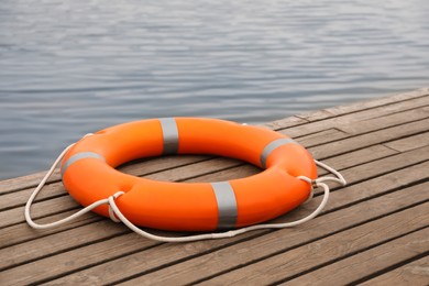 Photo of Orange lifebuoy on wooden pier near water. Rescue equipment