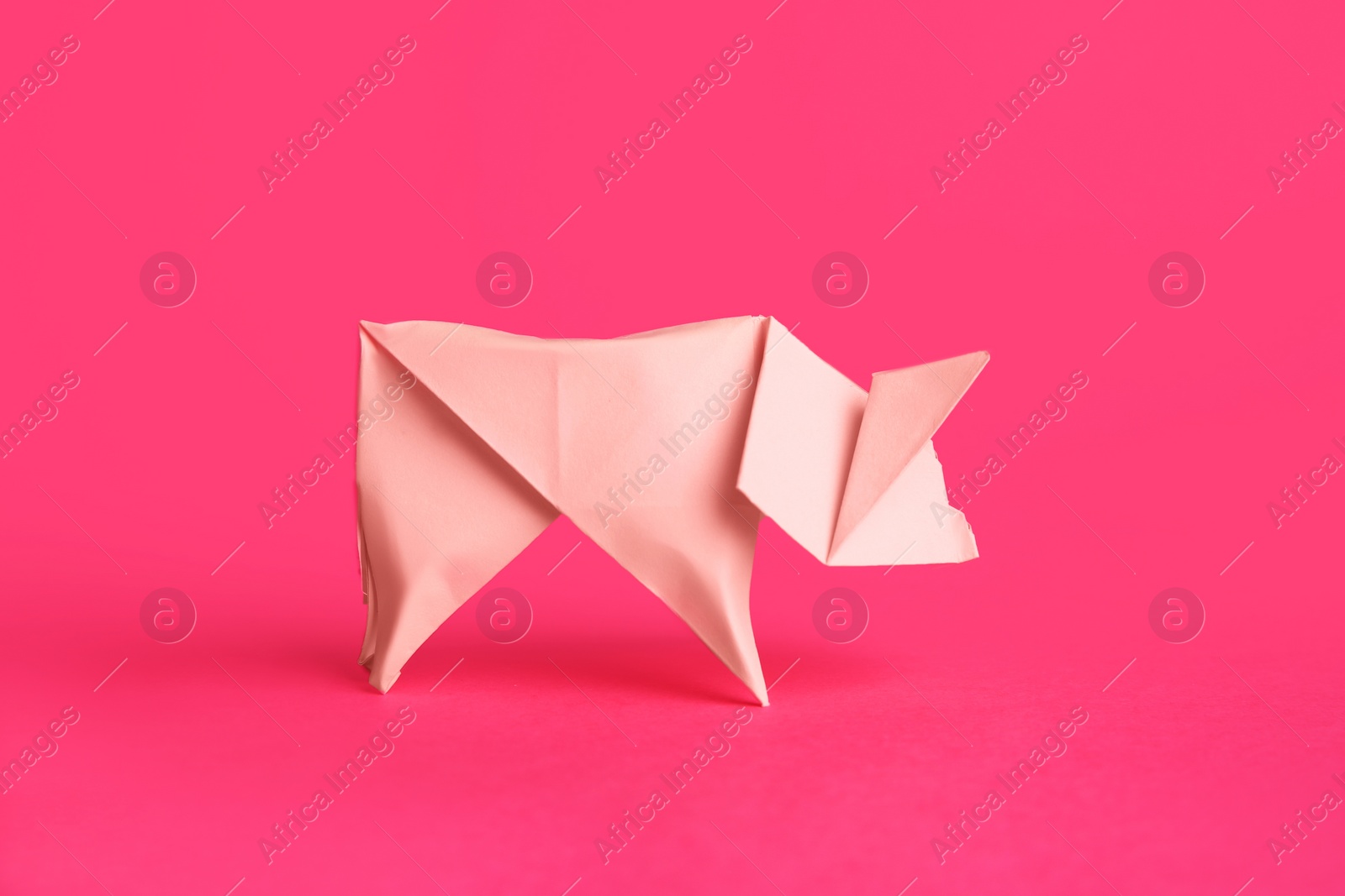Photo of Origami art. Handmade bright paper pig on pink background