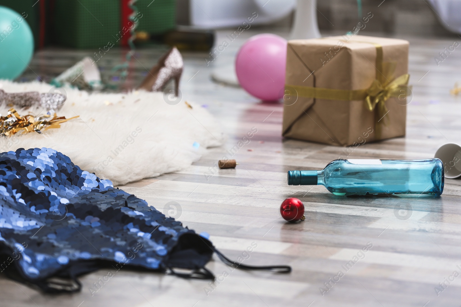 Photo of Empty bottle, dress and gift box on messy floor. Chaos after party