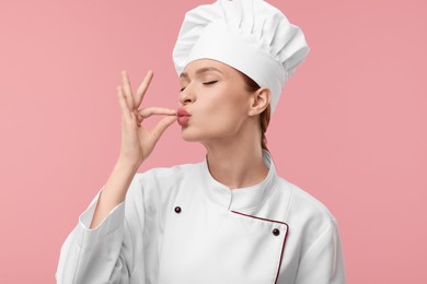Photo of Young woman chef in uniform showing perfect sign on pink background