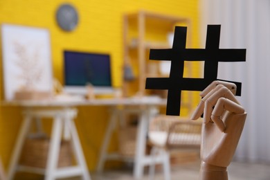 Photo of Wooden mannequin hand with paper hashtag symbol indoors. Space for text