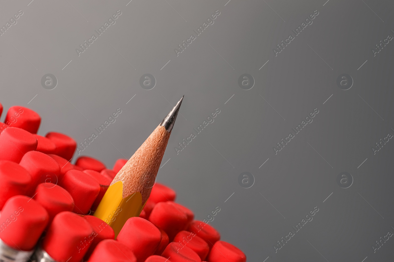 Photo of Sharp graphite pencil among others with erasers on grey background, closeup. Space for text