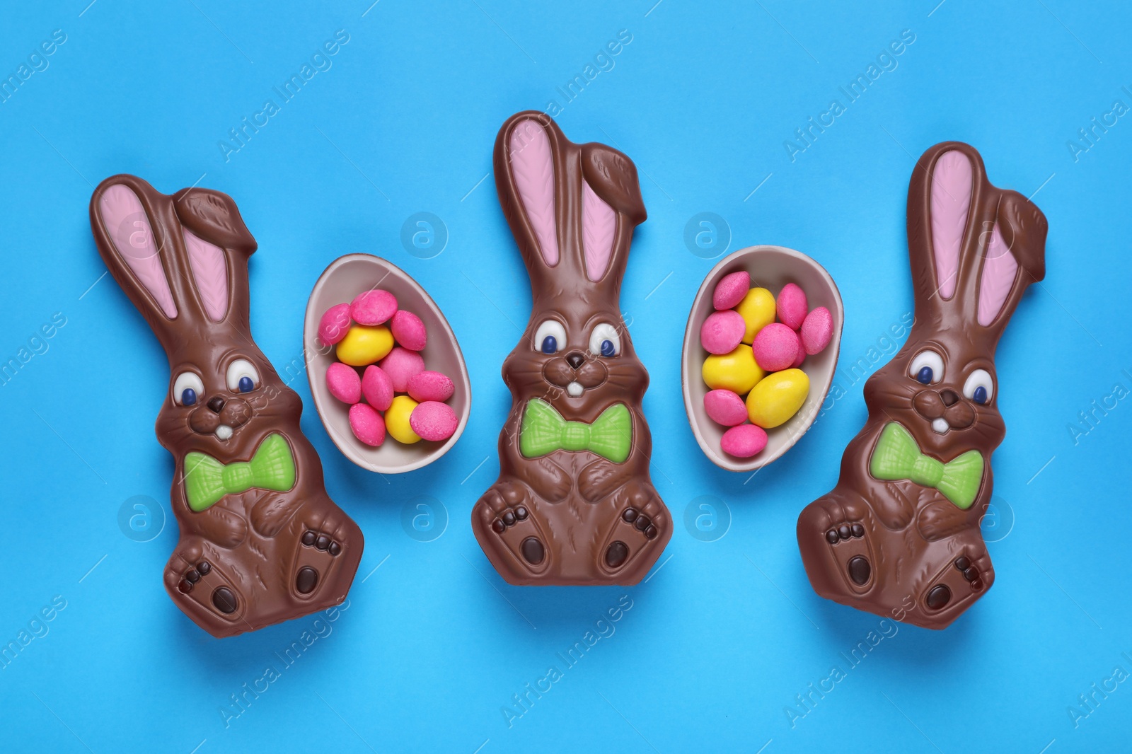 Photo of Chocolate Easter bunnies, halves of egg with candies on light blue background, flat lay